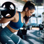 Young sportswoman working out with a barbell in health club.